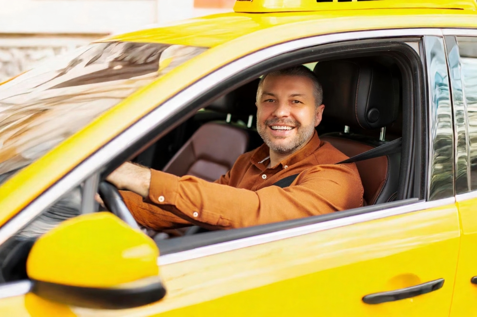 cheerful man driving yellow taxi car looking through open window smiling camera holding hands steering wheel 726520 4541 (1)